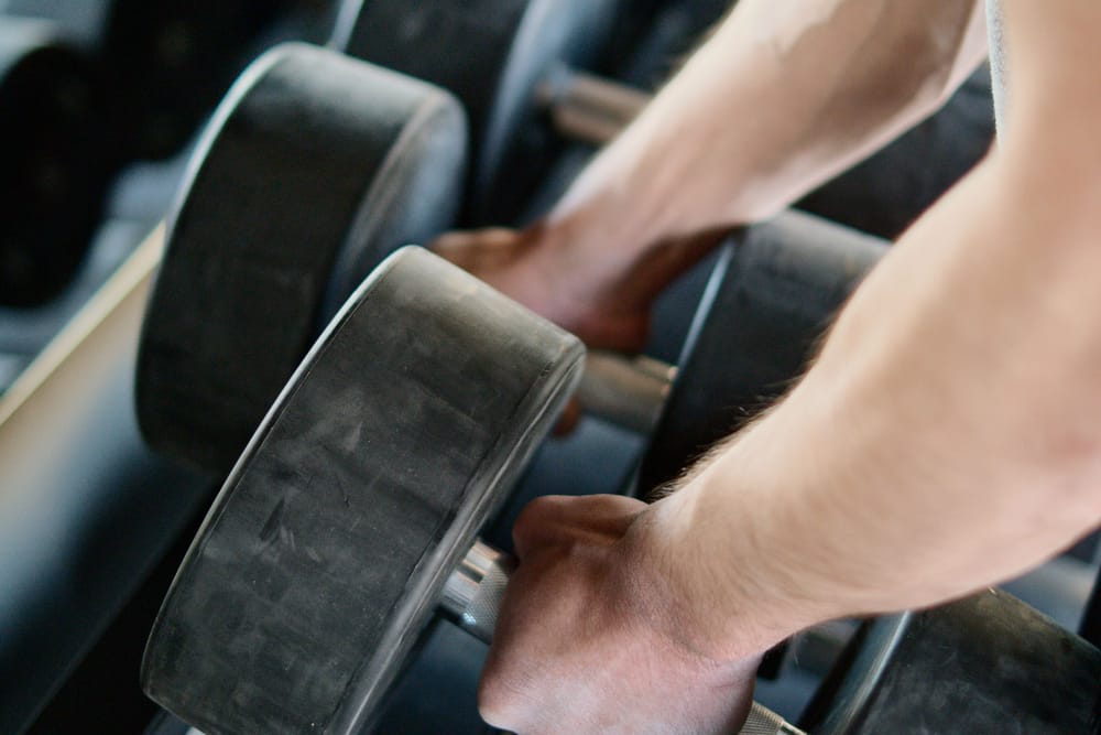 Hands selecting a dumbbell from a rack