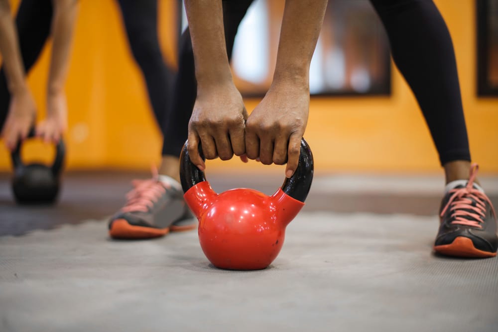 Low-framed training composition of hands holding a kettlebell, with faces outside the frame