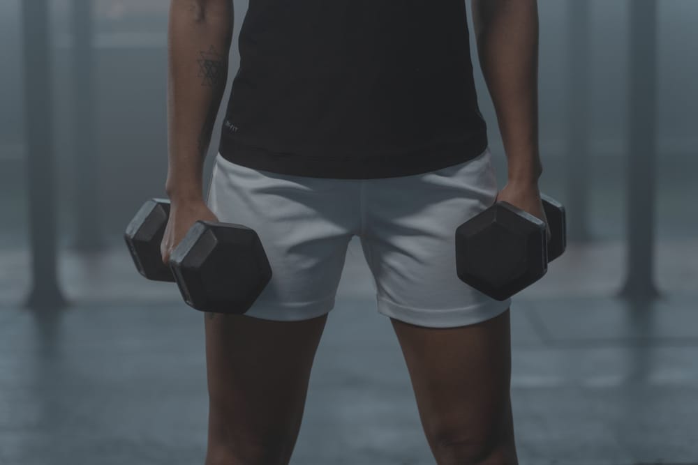 Faceless composition of a person holding dumbbells at their sides